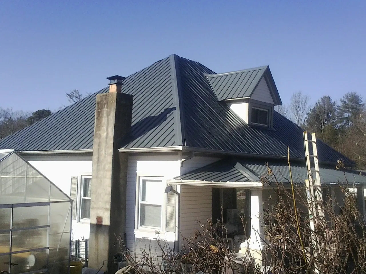 Dark blue standing seam metal roof on a white farmhouse with dormer — Slate & Tile Roof Repair by Roofing Brothers in Elliott