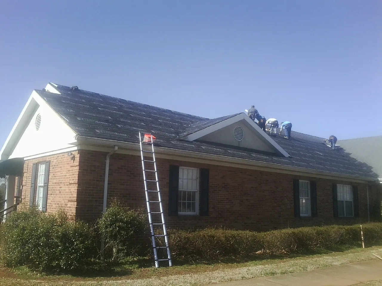 Crew tearing shingles off a brick ranch roof with a ladder set — Emergency Roof Repair work by our crew in Elliott