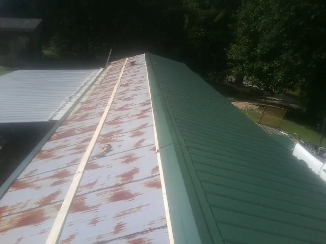 Old rusted panels beside newly installed green metal roofing — Wind Damage Roof Repair by Roofing Brothers in Elliott