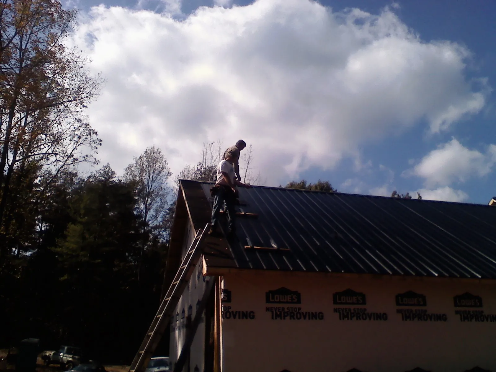 Roofer fastening dark metal panels high against a cloudy sky, from a Roof Inspection job in Elliott