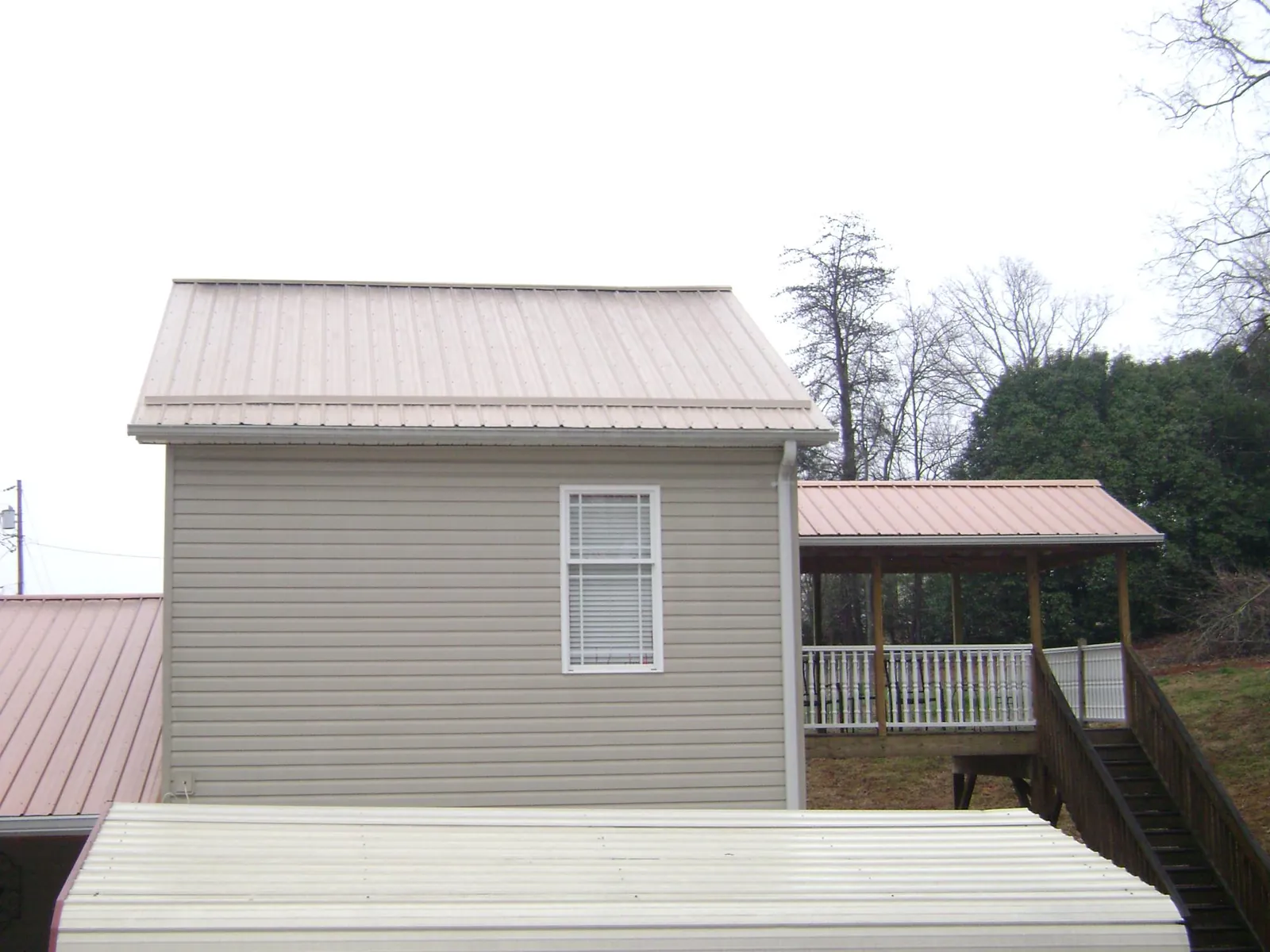 Tan metal roofs on a two story addition and attached porch, from a Roof Replacement job in Elliott
